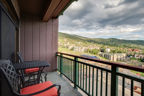 Sweeping mountain and valley vistas frame this private balcony retreat, where forested peaks meet charming alpine architecture below dramatic skies.
