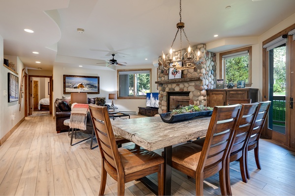 Gather around the stunning rustic dining table where natural light streams through garden views. The stone fireplace and open layout invite you to relax in comfort.