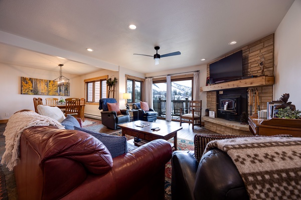 Settle into plush leather seating by the wood-burning fireplace as natural light floods through windows framing stunning mountain vistas. Warm woods and cozy textures create your perfect alpine retreat.