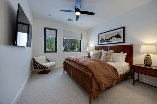 Unwind in your serene bedroom with a plush bed, modern ceiling fan, and peaceful views of the surrounding greenery through large windows.