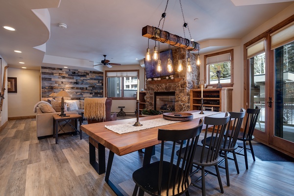 Gather around this stunning handcrafted table where rustic wood meets modern comfort. Natural light pours through expansive windows while the stone fireplace adds warmth to your mountain retreat.