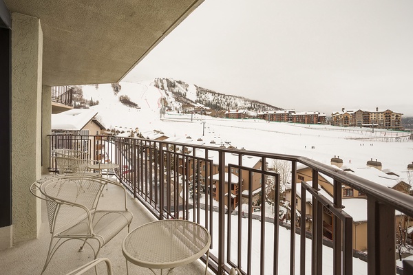 This expansive balcony frames a striking winter panorama of ski slopes, chairlifts, and alpine lodges. A scenic mountain resort setting awaits outside the property, perfect for winter sports enthusiasts.