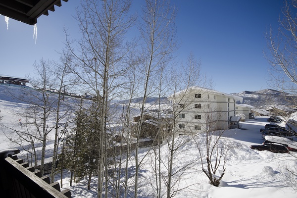 A winter mountain setting with snow-covered slopes and bare trees under clear blue skies, offering a peaceful ski resort atmosphere.