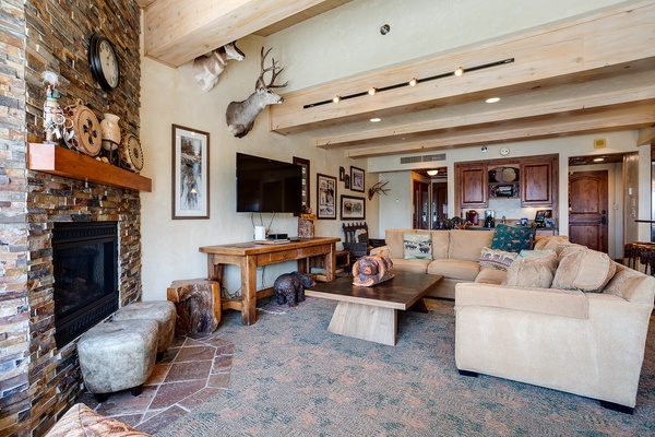 Picture yourself unwinding in this spacious living room, where rustic charm meets mountain luxury. Sink into plush sofas by the stone fireplace and enjoy your favorite shows on the flat-screen TV under vaulted wood-beam ceilings.