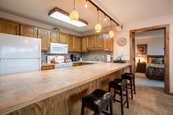 Picture yourself preparing meals in this well-equipped kitchen with warm wood cabinetry, tiled counters, full appliances, and a spacious breakfast bar for casual dining.