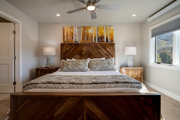 Drift off in this serene bedroom with a plush bed, warm wood accents, soft lighting, and stunning views framed by the window—your restful retreat awaits.