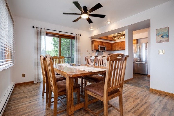 Gather around this inviting dining table for meals and memories. Natural light streams through the windows, while the open layout connects you to the fully-equipped kitchen—perfect for your mountain getaway.