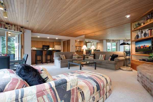 Unwind in your spacious open living area with warm wood ceilings, cozy seating, and mountain views just outside. The kitchen's nearby for easy entertaining.