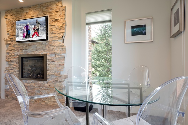 Gather around the sleek glass table by the stone fireplace, with mountain views and modern seating creating your perfect spot for meals and après-ski stories.