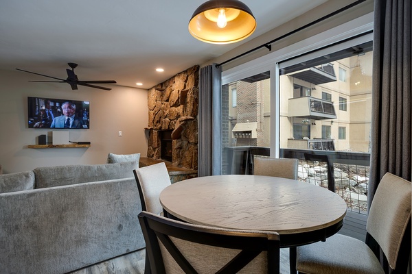 Unwind at your round dining table with mountain views and a cozy stone fireplace. Sunlight streams through floor-to-ceiling windows, illuminating your open-concept space designed for effortless comfort.