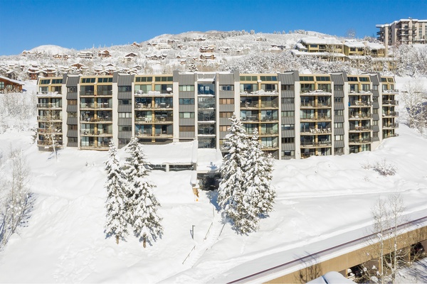 Modern apartment complex nestled in a pristine alpine ski resort, surrounded by snow-covered mountains and evergreens, offering an ideal winter getaway location.