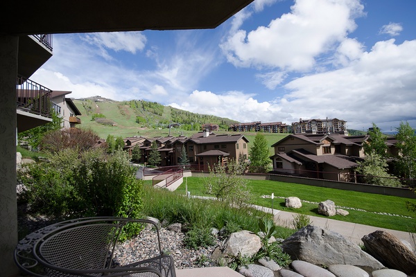 A mountain resort development nestled at the base of ski slopes, with multi-story residential buildings overlooking manicured grounds and natural landscaping in a scenic alpine valley.