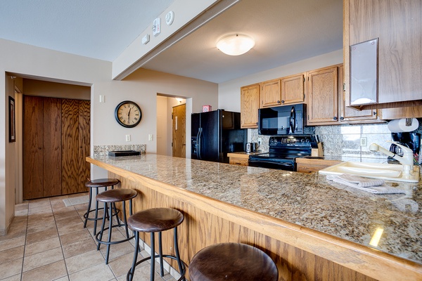 Gather around your spacious granite breakfast bar where morning coffee feels effortless. The fully equipped kitchen invites you to cook together, with sleek black appliances and plenty of counter space for meal prep and conversation.