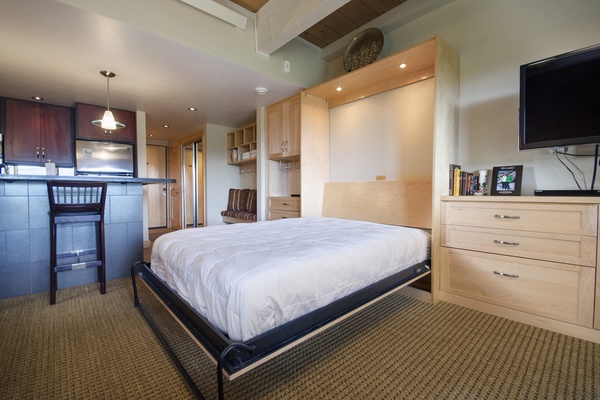 Unwind in your cozy studio retreat with a plush bed, smart storage, and a sleek kitchenette. Modern conveniences meet warm wood tones for the ultimate escape.