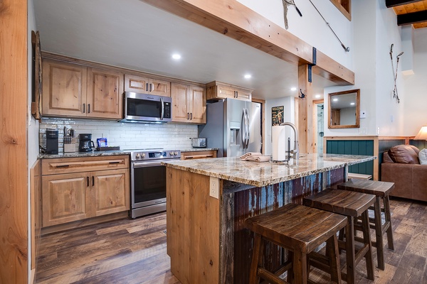 Your mountain retreat features a fully equipped gourmet kitchen with granite island seating, stainless appliances, and rustic wood accents beneath soaring timber-beam ceilings.