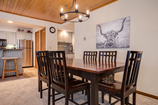 Gather around this inviting dining table where your group can share meals and make memories together. The rustic chandelier and warm wood ceiling add mountain charm to every dining experience.