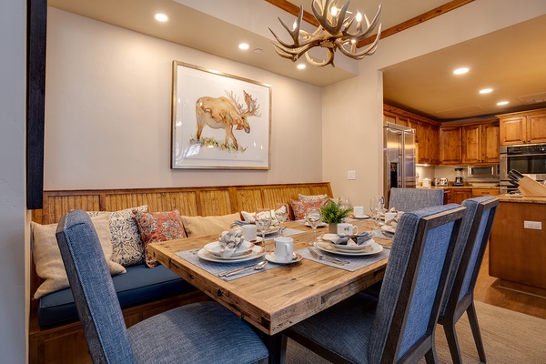 Gather around this warm dining space featuring rustic wood accents, comfortable seating, and a stunning antler chandelier overhead. The open layout flows into a fully-equipped kitchen, perfect for memorable meals together.