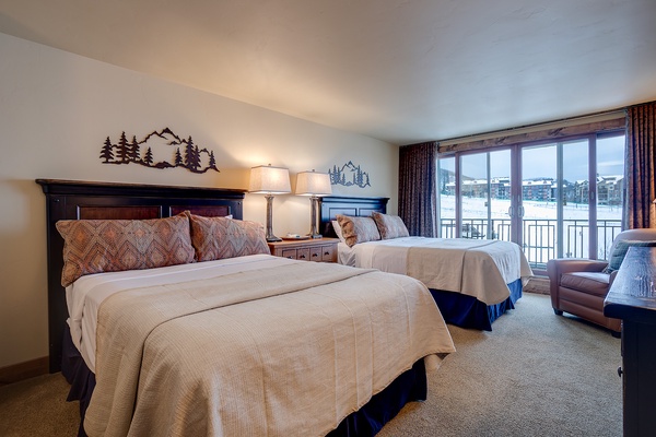 Wake up to serene winter views in this inviting bedroom with two plush beds, cozy mountain-inspired décor, and a private balcony overlooking snowy landscapes.