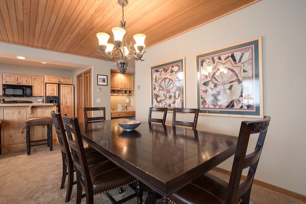 Step into your vacation dining space, where a warm wood ceiling and elegant chandelier create the perfect setting for shared meals and mountain memories around this spacious table.