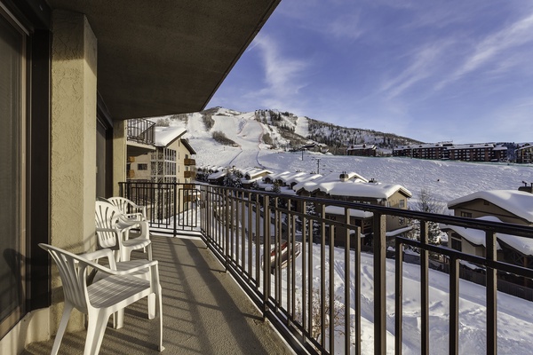 This property is located in a winter resort area with direct views of ski slopes and surrounding snow-covered buildings. The balcony provides a panoramic mountain setting.