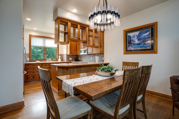 Gather around the warm wood table for meals in this inviting dining area, where rich cabinetry and a stunning chandelier create a cozy mountain retreat atmosphere.