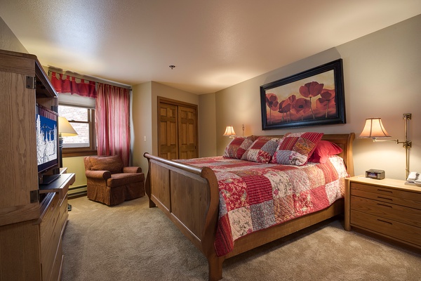 Settle into your cozy bedroom with warm wood furnishings, a plush quilted bed, and soft lighting that invites restful nights after mountain adventures.