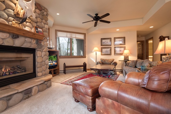 Unwind in your spacious living room with a cozy stone fireplace, plush leather seating, and warm lighting perfect for evenings after exploring nearby trails.