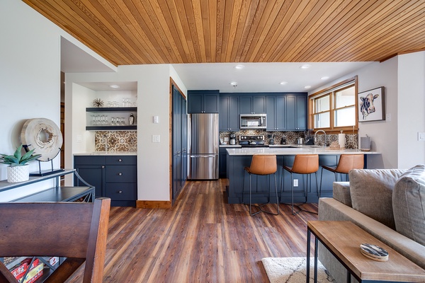 Your open-concept retreat welcomes you with rich wood floors, striking blue cabinetry, and a cozy breakfast bar—perfect for morning coffee or gathering with friends after a day of adventure.
