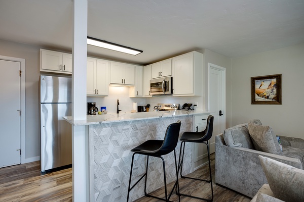 Your open-concept kitchen features white cabinetry, stainless steel appliances, and a stylish breakfast bar with marble-patterned tile backsplash—perfect for morning coffee or casual meals.
