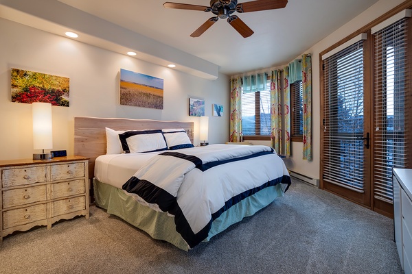 Sink into crisp linens and let the ceiling fan's gentle breeze lull you to sleep. Natural light floods through windows framing mountain views, while colorful artwork adds warmth to your peaceful retreat.