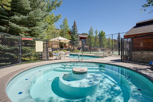 Soak in the bubbling hot tub under sunny skies, with lounge chairs and towering evergreens creating your perfect outdoor escape.