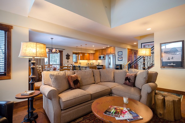 Settle into your spacious living area where plush seating and warm wood tones create an inviting retreat. Beyond, your fully equipped kitchen awaits, ready to make every meal at home feel special.