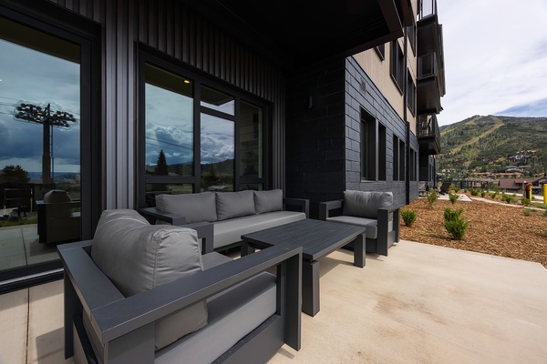 Modern mountain retreat featuring a covered patio with sleek outdoor furniture, perfect for relaxing while surrounded by stunning hillside views and fresh alpine air.