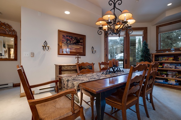 Gather around this inviting dining table where your group can share meals and stories beneath an elegant chandelier. Natural light pours in through windows that frame peaceful mountain views.