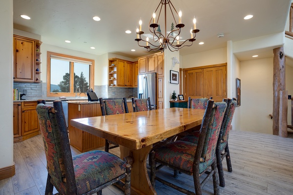 Gather around a handcrafted wood table under elegant chandelier light, with mountain views through the window. This warm, inviting dining space is perfect for shared meals and lasting memories.