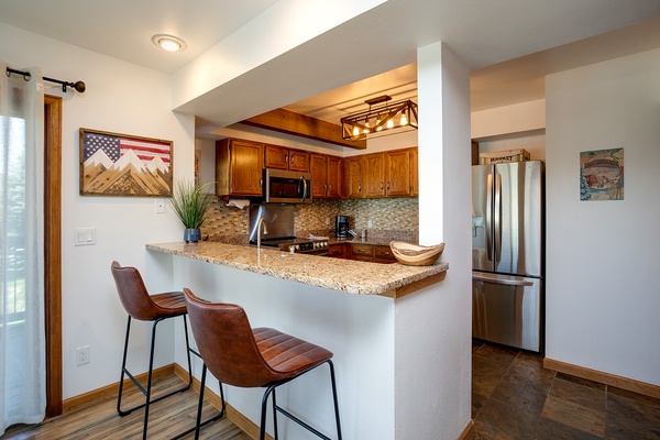 Pull up a seat at your granite breakfast bar and enjoy morning coffee in this well-appointed kitchen with warm wood cabinetry, modern appliances, and thoughtful lighting overhead.