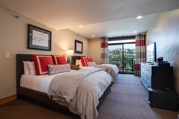 Two plush beds dressed in soft linens and bold red accents await you in this spacious bedroom, complete with a balcony overlooking the surrounding neighborhood and modern entertainment amenities.