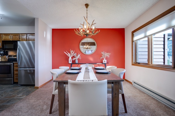 Gather around this rustic dining table beneath a stunning antler chandelier. Your meals become mountain memories with bold red décor, natural light streaming through windows, and seating for six ready for laughter and connection.