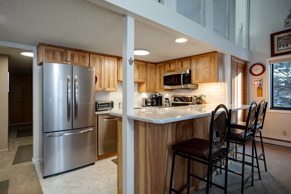 Your fully equipped kitchen features stainless steel appliances, warm wood cabinets, and a breakfast bar perfect for morning coffee or casual meals together.