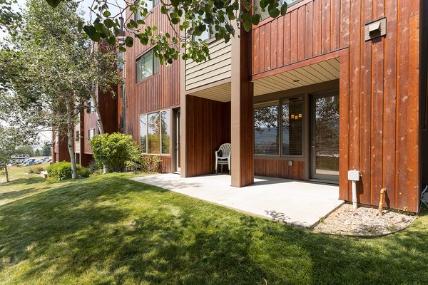 Charming wood-paneled exterior with private patio and lush green lawn, framed by mature trees and offering peaceful waterfront glimpses—your perfect retreat awaits.