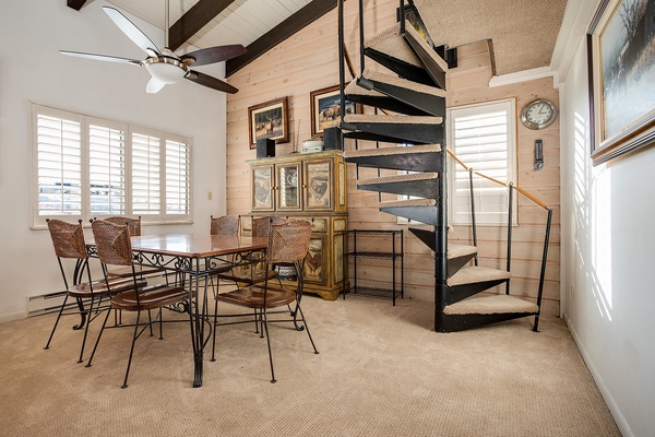Picture yourself gathered around this inviting dining table, sunlight streaming through plantation shutters, with a charming spiral staircase leading to your cozy loft retreat above.