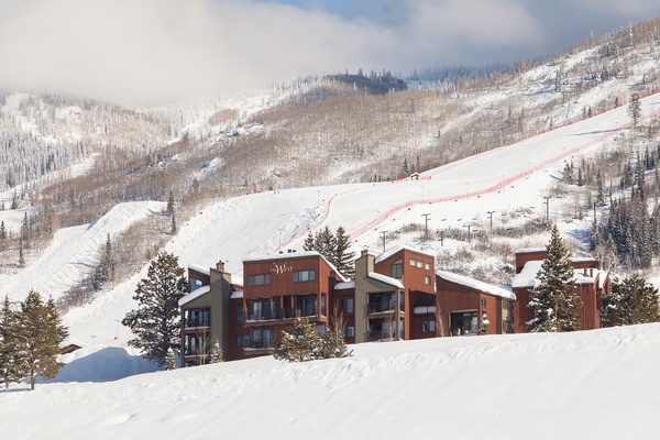 A snow-covered mountain lodge nestled near ski slopes, with chairlifts and pristine powder-covered terrain stretching across the peaks—an ideal winter escape for alpine adventure.
