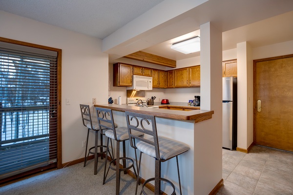 Gather at your breakfast bar with morning coffee, where warm wood cabinetry and a fully equipped kitchen invite you to cook and connect in relaxed comfort.