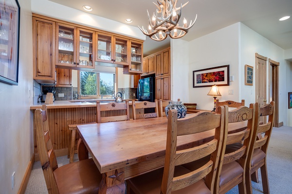 Gather around this handcrafted wooden table beneath a stunning antler chandelier, where your family meals become cherished mountain memories in this warm, open kitchen and dining space.