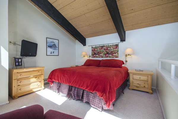 Drift off under charming exposed beams with warm bedside lamps casting a soft glow. Your cozy retreat features a plush red bedspread, mountain-inspired art, and entertainment at your fingertips.