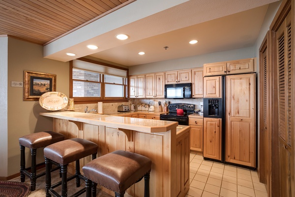 Your fully equipped kitchen features warm wood cabinetry, stainless appliances, and a breakfast bar with three stools—perfect for morning coffee or casual meals together.