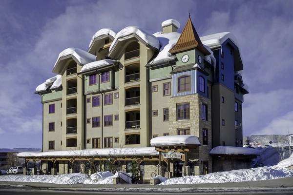 A distinctive alpine-style building with a clock tower stands proudly in a snow-covered mountain setting, marking the entrance to the property.