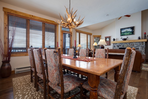 Gather around this handcrafted dining table under a stunning antler chandelier. Large windows frame mountain views, while the stone fireplace adds warmth to your group meals and memorable evenings together.
