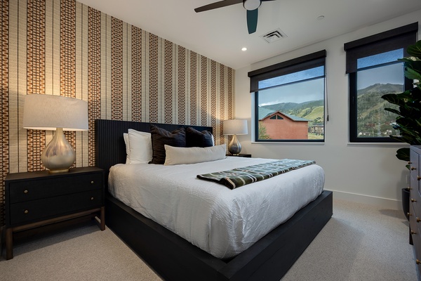 Drift off in crisp linens beneath a striking textured accent wall, with mountain views framing your mornings through large windows. Your peaceful retreat awaits with stylish furnishings and a serene ambiance.