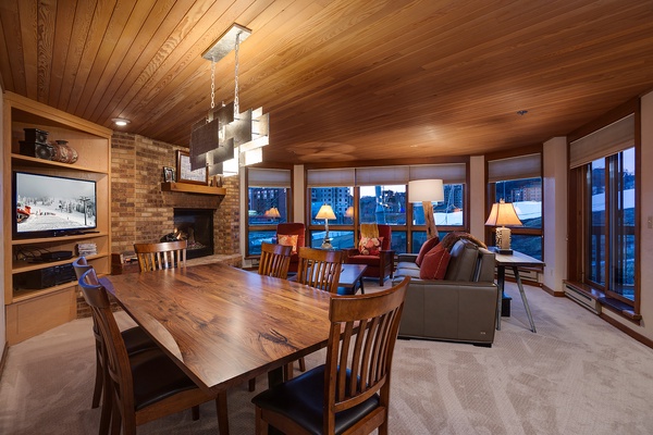 Gather with loved ones in this warm, wood-paneled retreat featuring a cozy fireplace, spacious dining table, and stunning mountain views through expansive windows.